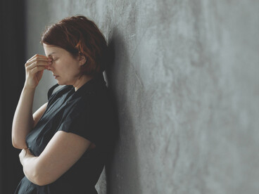 A distressed woman leaning against a concrete wall, reflecting emotional strain and a sense of isolation