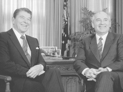 President Ronald Reagan (left) sitting down and smiling in the Oval Office with Soviet leader Mikhail Gorbachev in 1987