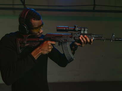 Homem realiza treinamento de tiro com uma Kalashnikov AKM, arma utilizada pelas forças policiais moçambicanas. O artigo discute o peso das armas na manutenção do poder