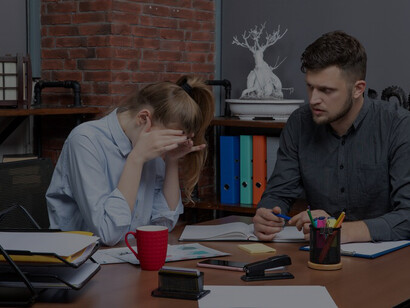 Young female and male co-worker seated at a table, displaying signs of fatigue in the office, emphasizing the negative impact of a challenging workplace environment and the importance of addressing exhaustion