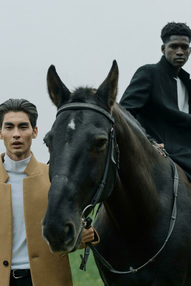 Young male fashion models standing beside a horse