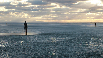 Antony Gormley  Another Place, 1997, Antony Gormley’s Another Place features 100 cast-iron figures facing the sea along Crosby Beach, exploring humanity’s relationship with nature, time, solitude, and existence. Each life-sized figure, modelled on Gormley’s own body, stands motionless against shifting tides and weather, symbolizing reflection, resilience, and the universal human search for meaning and connection
