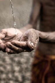 A frail, emaciated man with parched, weathered hands desperately cups a trickle of water against a backdrop of cracked, barren earth—a haunting symbol of extreme drought and deprivation, reflecting the dire consequences of ineffective development aid
