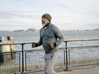 A bearded man dressed for cold jogging near a river