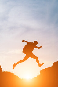 As the sun sets behind him, the man leaps across the rocks, embracing the journey, not just the destination, in his pursuit of personal growth