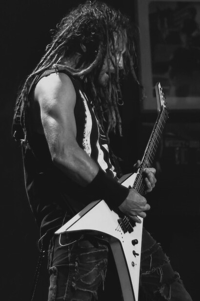 A man in a black t-shirt passionately playing the guitar on a brightly lit stage