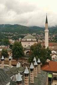 Vista Panorâmica Da Arquitetura Histórica De Sarajevo. Ao chegar a Sarajevo, fui imediatamente arrebatada pela paisagem que circunda a cidade e pela arquitetura variada, refletindo séculos de dominação otomana, austro-húngara e, mais recentemente, os traços deixados pela antiga Iugoslávia. Caminhar por suas ruas é como folhear as páginas de um livro de história vivo
