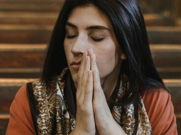 A brunette woman kneels in a church as she prays