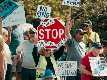 Demonstrators gathering with messages defending democracy and collective action, reflecting the public pushback against authoritarian ideas and political overreach