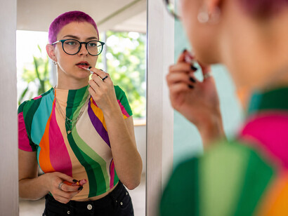 Stylish young woman with vibrant pink hair doing her makeup in a brightly lit room