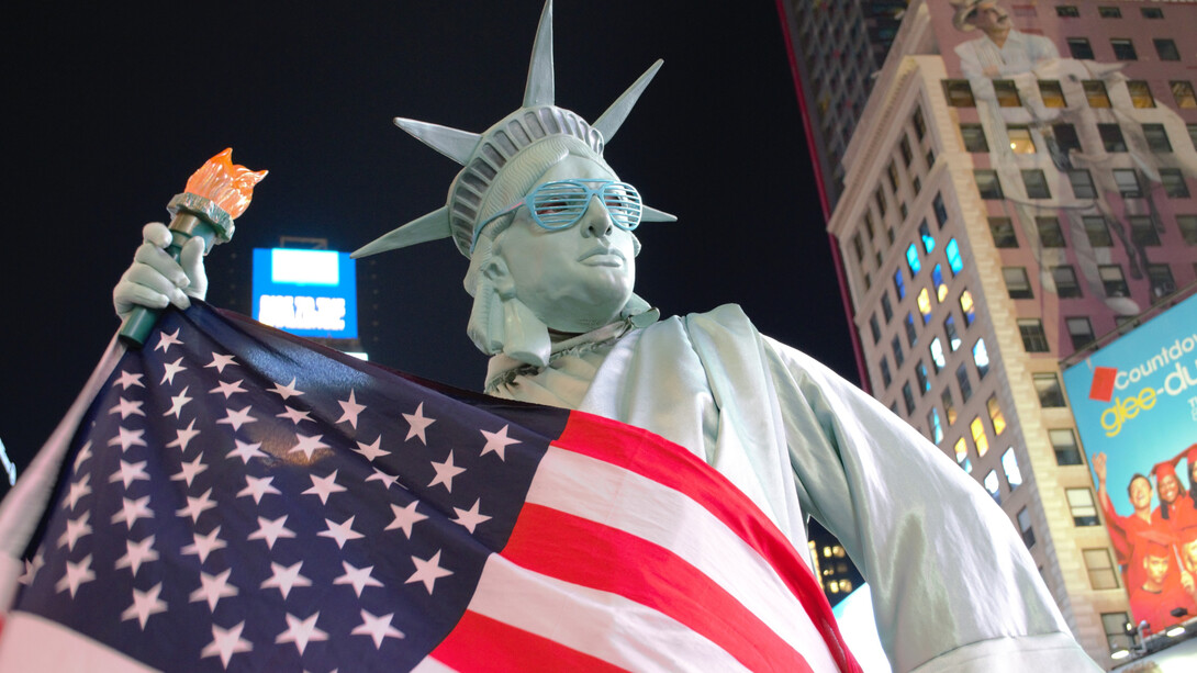 The Statue of Liberty draped in the American flag, wearing sunglasses