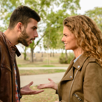 A man and woman in brown jackets stand near a tree, arguing and looking away from each other—capturing emotional distance and loneliness in their relationship