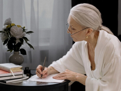 A thoughtful senior woman writes a letter with a fountain pen while sitting at her desk