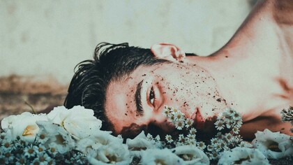 A man lies down next to daisies, looking upset