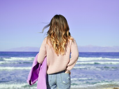 A woman stands at the shoreline, gazing at the endless horizon, with the rhythmic crashing of the waves and the salty air offering a moment of serenity and reminding us that nature has a way of quieting the mind and restoring the soul
