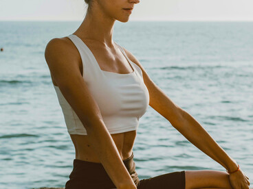 An adult woman practices meditation on a yoga mat by the sea, embracing the calmness and stillness of the outdoors