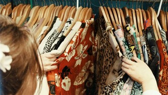 A woman rummages through a rack of colorful clothes at a thrift store