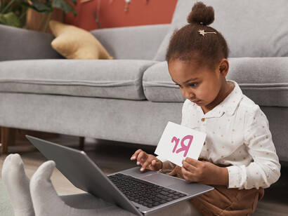 Criança em processo de alfabetização mostra a inicial de seu nome para a aula online