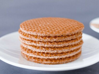Stroopwafels on a white ceramic plate, accompanied by a warm drink in a white ceramic mug