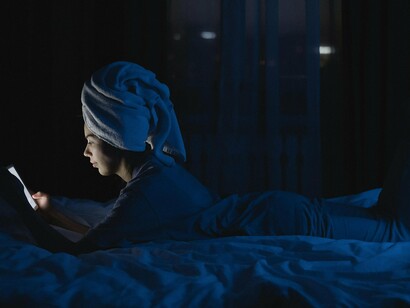 A woman using her phone while resting on her bed at night, conveying the blurred boundary between rest and digital compulsion