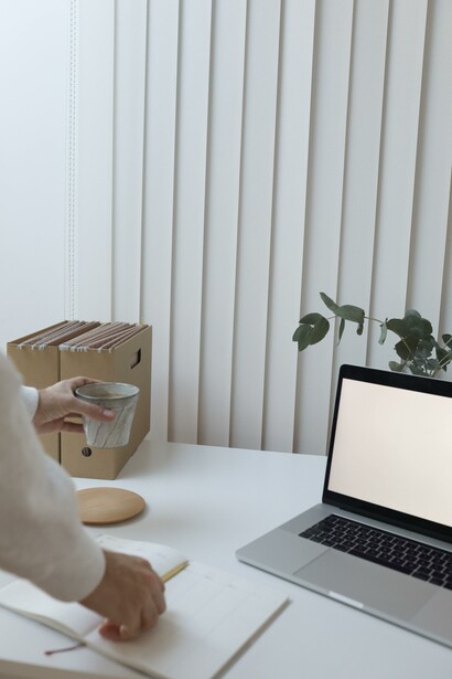 A woman placing a coffee on a table next to a laptop