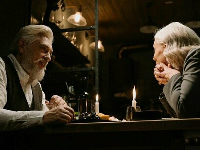 An old couple seated together at a simple dining table, gazing at each other fondly, symbolising devotion shaped by time rather than perfection