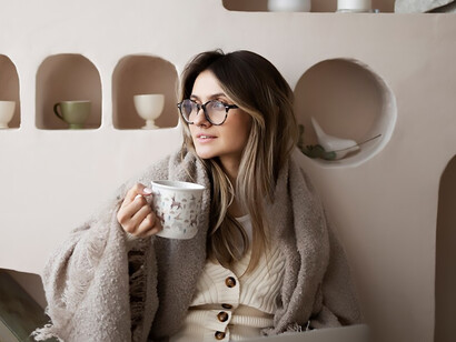Wrapped in winter coziness, a woman sips her coffee, embracing the warmth of the season in her comfy attire