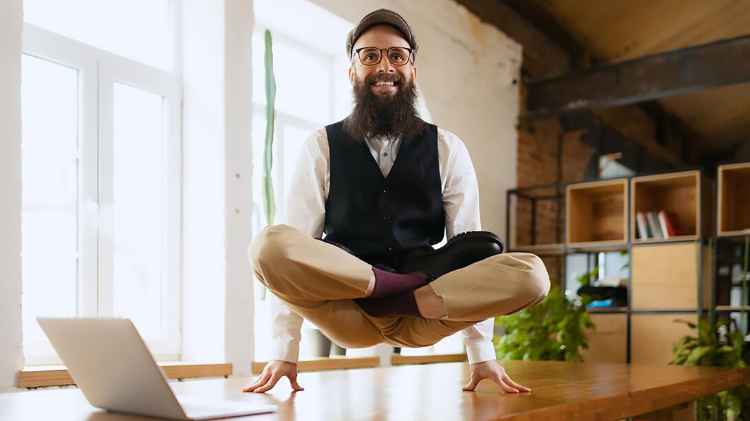 In a modern office, a smiling businessman practices relaxation techniques while sitting at his desk with his hands resting comfortably