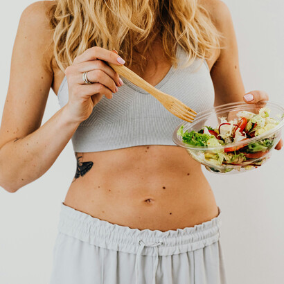 A toned woman eating a vegetable salad and tracking calories for a healthy lifestyle