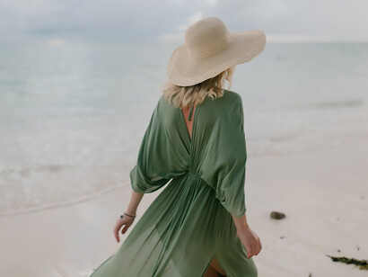 Under the sweeping gusts of a windy day, a woman strolls along the wet sandy beach, her steps leaving imprints as the sea breeze plays with her hair