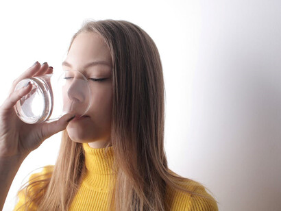 A health-conscious woman in a bright yellow t-shirt sipping water to stay hydrated and combat dehydration