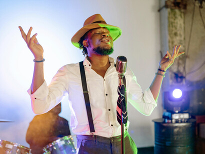 A man wearing a hat sings with a band in a classic-style concert, capturing artistic expression, rhythm, and raw energy