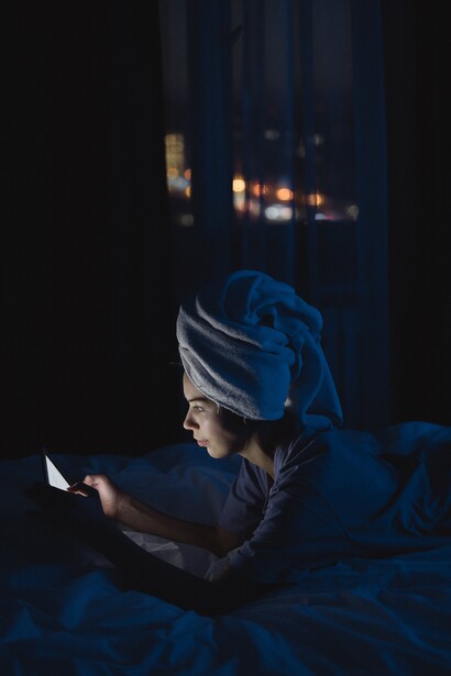 A woman lying on a bed in a dark room looking at a mobile phone