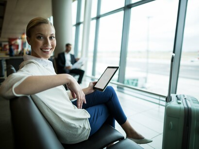 A smiling traveler lounges at the airport with a tablet in hand, reflecting the article’s focus on staying organized and relaxed while on the move
