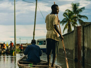 A resident steering a wooden boat through floodwaters, representing the daily reality of communities adapting to increasingly severe flooding