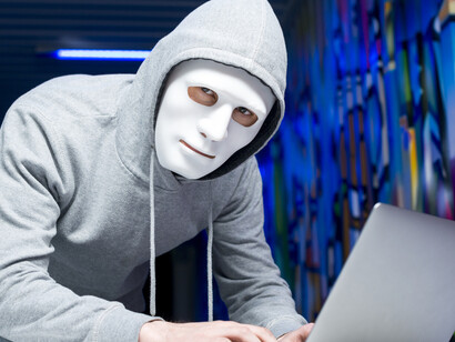 Hacker wearing a mask and hoodie while using a computer