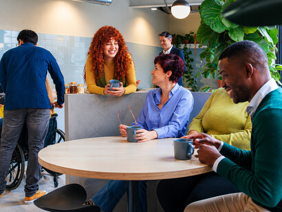 A diverse team of professionals enjoys a coffee break in a modern office, reflecting cultural diversity and workplace inclusion