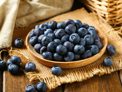 Fresh, ripe blueberries spill from a woven basket onto a weathered wooden table