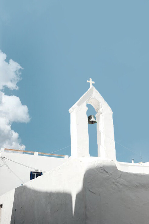The elegant bell tower of a whitewashed church stands majestically against the backdrop of Naxos, Greece