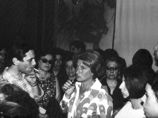 Dirigente sindical entrevistada por Juan Pablo Renzi y rodeada de público. En el fondo una fotografía ampliada de la represión policial en Tucumán, Argentina. Noviembre de 1968