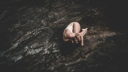 Uma mulher permanece encolhida sobre uma superfície áspera, em uma postura que transmite vulnerabilidade e sofrimento. Quando emoções permanecem silenciadas por muito tempo, o corpo pode transformar esse silêncio em sinais que pedem atenção e cuidado. A imagem de uma mulher encolhida sobre uma superfície rochosa busca transmitir vulnerabilidade, sofrimento, recolhimento e tensão emocional, funcionando como uma metáfora visual para o momento em que o corpo passa a expressar aquilo que a mente não conseguiu elaborar. Ansiedade, tensão e outros sintomas físicos podem revelar conflitos emocionais que ainda buscam um caminho de elaboração. Escutar o que o corpo comunica não significa ignorar a medicina, mas reconhecer que algumas dores também carregam histórias que precisam ser compreendidas