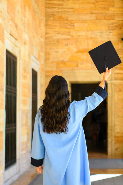 With her graduation hat in hand, a brunette woman pauses in contemplation — a symbol of accomplishment and new beginnings