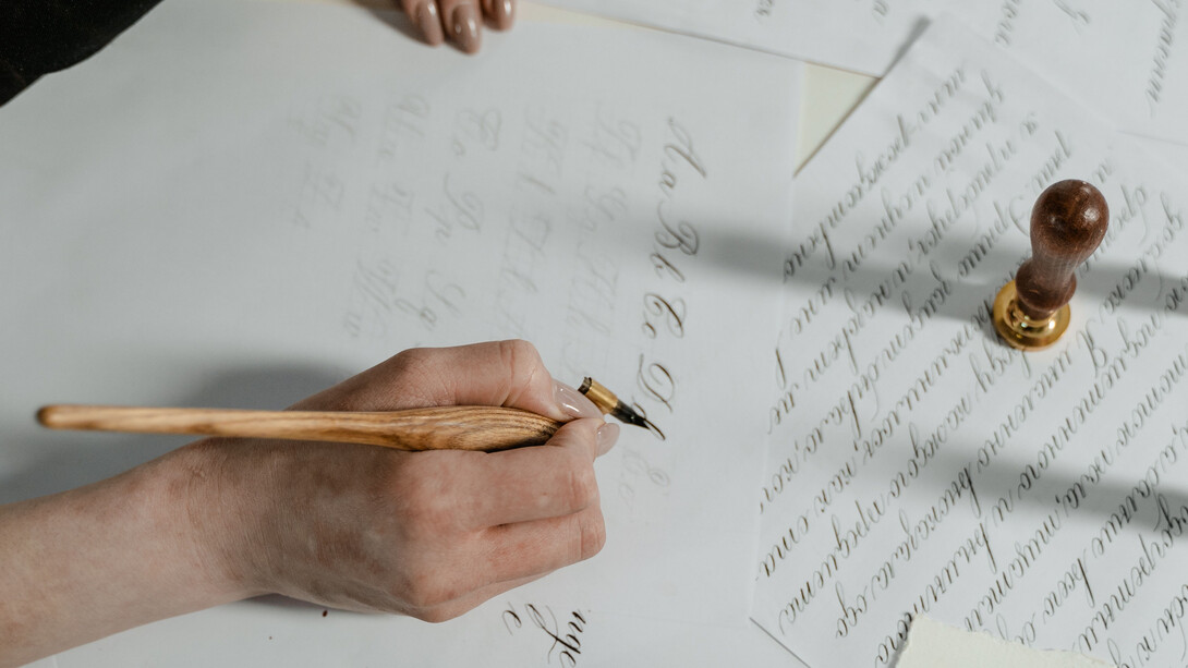 Mão de uma escritora transferindo tinta da caneta ao papel para iniciar uma história