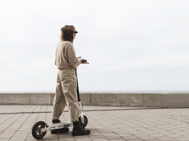 A young woman commuting on an electric scooter through a calm, pedestrian-friendly urban environment