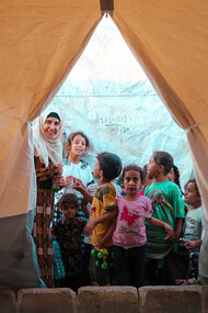 Displaced by conflict in the Middle East, a group of refugees gathers inside a tent