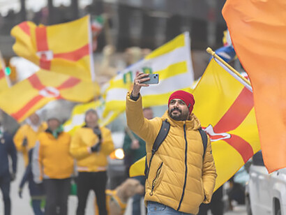 At the Saint Patrick's Day parade, a man captures the moment with a festive selfie, surrounded by a group proudly marching with County Antrim flags
