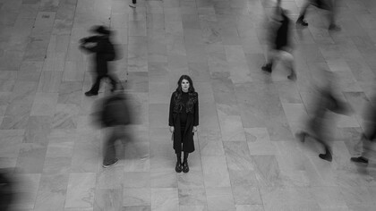 A solitary woman standing alone in a busy New York terminal, capturing the contrast between personal loneliness and the surrounding crowd, USA