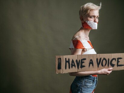 Woman with a taped mouth, holding  sign that reads: I have a voice