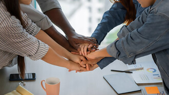 Colleagues working together, enthusiastically joining fists in a show of teamwork and collaboration