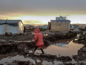 In Idlib, Idlib Governorate, Syria, people gather around rows of tents in a refugee camp, set against muddy and challenging conditions